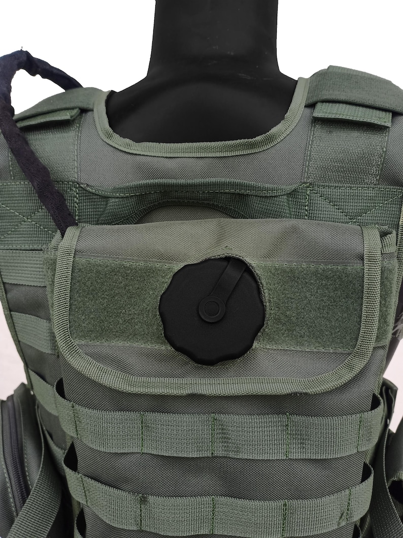 May include: Olive green tactical vest with multiple straps and pouches. Features a black hydration reservoir cap and a black hose. The vest is designed for military or outdoor activities.