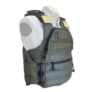 Puede incluir: Un chaleco táctico verde oliva con múltiples bolsillos y correas MOLLE. El chaleco tiene una cremallera negra y se muestra sobre una camisa blanca. Una insignia dorada es visible en el hombro derecho.