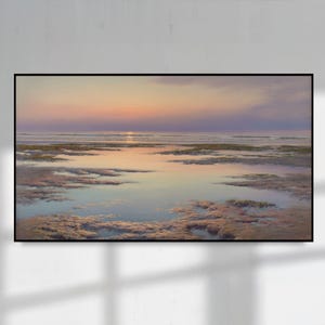 May include: A framed landscape painting depicts a serene coastal scene at sunset. The sky transitions from soft pinks and oranges to purples, reflecting on the calm water. The foreground shows textured, shallow water and sand.