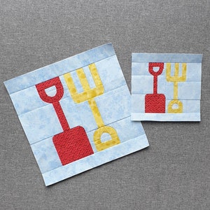 Peut inclure: Deux formes d'applique en tissu rouge et jaune d'une pelle et d'un râteau sur un fond bleu. Les formes sont cousues sur un carré de tissu bleu.