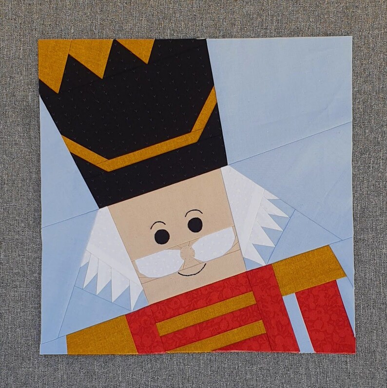 May include: A colorful paper pieced nutcracker with a black hat, white beard, and red and gold uniform.