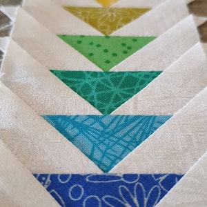 May include: A quilt block with a series of colorful triangles arranged in a chevron pattern. The triangles are in shades of pink, red, orange, yellow, green, blue, and white.