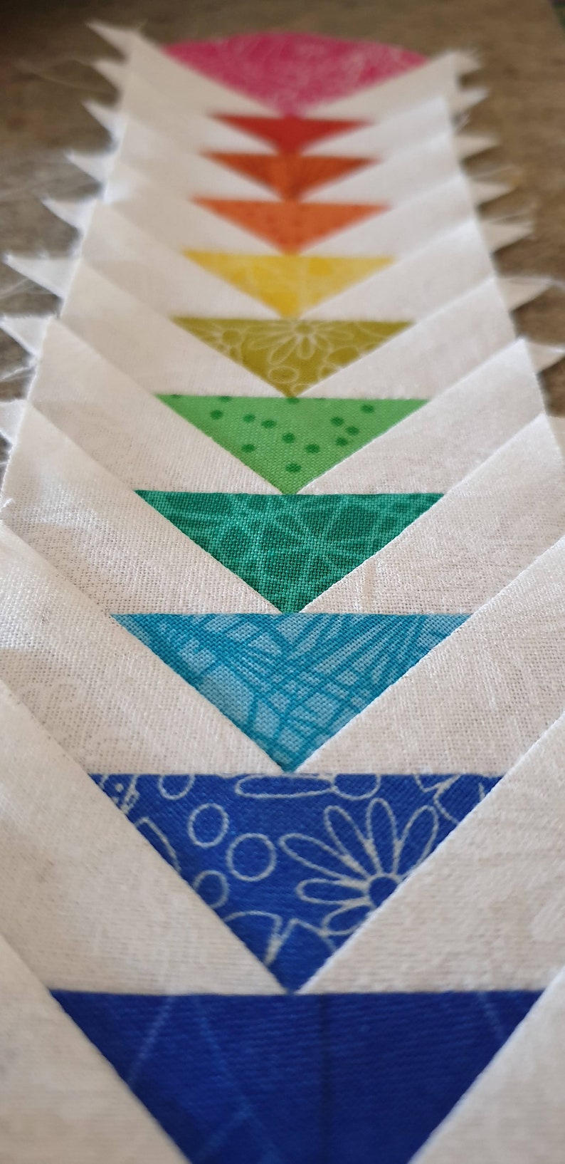 May include: A quilt block with a series of colorful triangles arranged in a chevron pattern. The triangles are in shades of pink, red, orange, yellow, green, blue, and white.