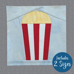 Peut inclure: Un bloc de courtepointe représentant un seau de popcorn à rayures rouges et blanches avec un dessus jaune. Le bloc est sur un fond bleu clair. Le texte "Includes 2 Sizes" est visible dans le coin inférieur droit.