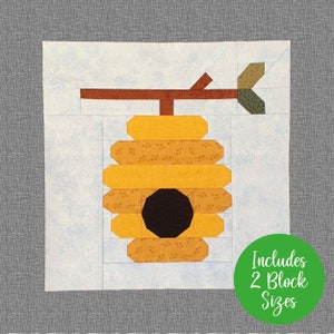 Könnte beinhalten: Ein Quiltblockmuster mit einem Bienenstock mit einem Zweig und einem Blatt. Der Bienenstock ist gelb mit einem schwarzen Eingang und besteht aus mehreren Schichten. Das Muster umfasst zwei Blockgrößen.