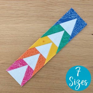 Può includere: Segnalibro in tessuto fatto a mano con un design a freccia geometrica. Il segnalibro presenta triangoli bianchi su uno sfondo arcobaleno di tessuti fantasia, tra cui rosa, arancione, giallo, verde e blu. Un cerchio blu con il testo "7 Sizes" è nell'immagine.