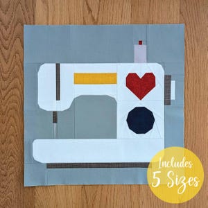 Può includere: Un blocco di trapuntatura con un design di macchina da cucire bianca con un cuore rosso e un ottagono nero. La macchina ha una striscia gialla ed è ambientata su uno sfondo grigio. Il testo "Includes 5 Sizes" è in un cerchio giallo.