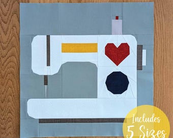 Könnte beinhalten: Ein Quiltblock mit einem weißen Nähmaschinen-Design mit einem roten Herzen und einem schwarzen Achteck. Die Maschine hat einen gelben Streifen und ist vor einem grauen Hintergrund platziert. Der Text "Includes 5 Sizes" befindet sich in einem gelben Kreis.
