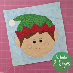 May include: A fabric elf face with a green hat, red trim, and a light blue background. The elf has black button eyes, a smiling red mouth, and rosy cheeks. The image includes the text "Includes 2 Sizes" in a green circle.