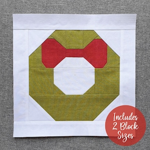 May include: A green and red patchwork quilt block in the shape of a wreath. The wreath is made up of squares and rectangles. The text "Includes 2 Block Sizes" is visible in the lower right corner of the image.
