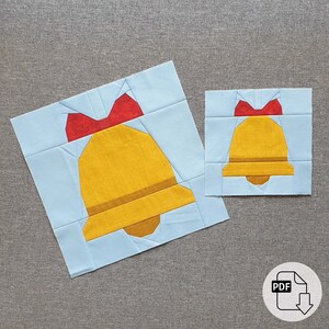 Op de afbeelding: Twee papieren patchwork patronen voor een kerstbel. Het grotere patroon is op een lichtblauwe achtergrond en het kleinere patroon is op een witte achtergrond. Beide patronen tonen een gele bel met een rode strik.