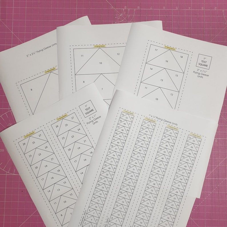 May include: Four sheets of paper with black lines outlining different sizes of flying geese quilt blocks. The sheets are labeled with the size of the finished square and the dimensions of the flying geese units. The sheets are on a pink cutting mat.