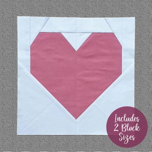 May include: A pink heart-shaped fabric block with white fabric surrounding it. The text "Includes 2 Block Sizes" is in a circle on the bottom right corner of the image.