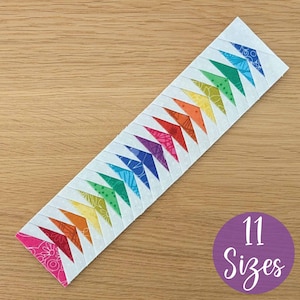May include: A rectangular quilt block with a repeating rainbow chevron pattern. Each chevron is a different color, including pink, orange, yellow, green, blue, and purple. The text "11 Sizes" is in a purple circle.