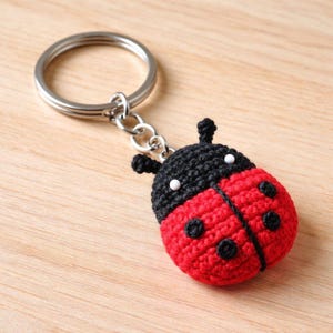 May include: A handmade ladybug keychain. The ladybug is crocheted with red and black yarn, featuring black spots and white accents. The keychain has a silver metal ring and chain.