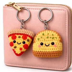 May include: Two crocheted food keyrings: a pizza slice and a burger. The pizza slice is yellow with red pepperoni and a brown crust. The burger is yellow and brown with green detailing. Both have smiling faces and are attached to silver keyrings.