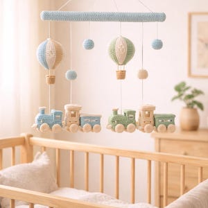 Peut inclure: Mobile de bébé fait à la main en crochet, avec une barre bleu clair. Il comprend deux montgolfières bleues et vertes, et deux trains bleus et verts. Des sphères bleues et beiges supplémentaires sont suspendues.