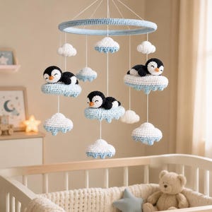 Puede incluir: Móvil para bebé hecho a mano con pingüinos de ganchillo sobre nubes. El móvil tiene un anillo azul claro y está suspendido sobre una cuna. Los pingüinos son negros y blancos, y las nubes son blancas y azul claro.