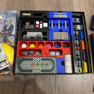 May include: A board game with a colorful game board, red, blue, and green game pieces, and a variety of cards. The game board has a track with spaces for the game pieces to move around. The game board also has a number of different areas for players to place their cards.