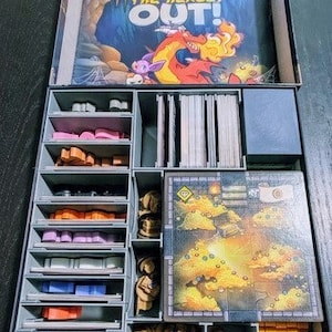 May include: A gray and black organizer with multiple compartments for storing game pieces. The organizer has a compartment for a game board with the text "Keep the Heroes Out!" on it.