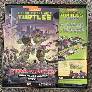 Puede incluir: Caja de juego de mesa Teenage Mutant Ninja Turtles City Fall con una portada de cómic que presenta a las cuatro tortugas en acción. La caja incluye un tablero de juego, cartas y miniaturas. El juego está basado en la popular serie de dibujos animados de Nickelodeon.