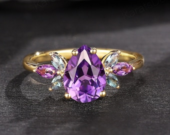 May include: A gold ring with a pear-shaped amethyst gemstone surrounded by smaller amethyst and blue topaz gemstones.