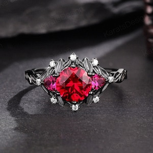 May include: Black ring with a large red gemstone surrounded by smaller white gemstones and black leaf-like accents.