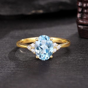 May include: A gold ring with a large oval-shaped blue topaz gemstone surrounded by smaller diamonds. The ring is set on a black background.