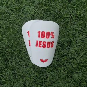 Könnte beinhalten: Zwei weiße, rechteckige, Vinyl-Aufkleber mit abgerundeten Ecken. Der obere Aufkleber hat den Text "100% JESUS" in roten Buchstaben. Der untere Aufkleber hat die Nummer "1" in roten Buchstaben. Beide Aufkleber haben ein rotes, stilisiertes Flügellogo.
