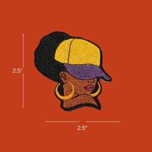 May include: Embroidered patch featuring a stylized Black woman wearing a yellow and purple baseball cap and gold hoop earrings. The patch measures 2.5 inches by 2.5 inches.