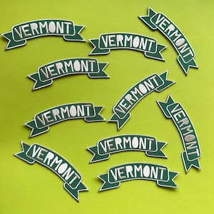 Könnte beinhalten: Neun grüne und weiße gestickte Bügelbilder mit dem Wort "VERMONT" in einem Banner-Design.