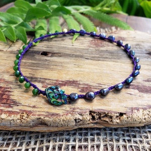 May include: A purple cord necklace with black and green beads and a large abalone shell pendant.