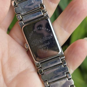 Op de afbeelding: Close-up van een zilverkleurig Brighton-horloge. Het horloge heeft een rechthoekige wijzerplaat met de merknaam en het woord "Istanbul" erop gedrukt. De horlogeband is gemaakt van rechthoekige schakels.