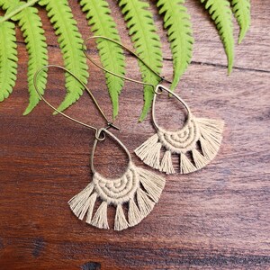 May include: A pair of beige macrame earrings with a fringe detail hanging from gold-toned hoops.
