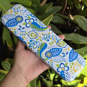 May include: A rectangular metal case with rounded corners featuring a white background and a repeating pattern of blue, light blue, and lime green floral and leaf motifs. The word Brighton is printed in a cursive script on the surface.