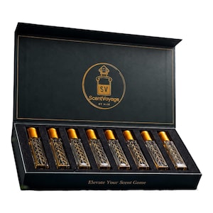 May include: A black rectangular gift box containing eight clear glass perfume roller bottles with gold caps. The interior lid features a gold circular logo with the text ScentVoyage BY M4H. The front of the box displays the text Elevate Your Scent Game.
