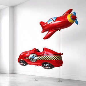 May include: Two red foil balloons: a race car with a lightning bolt emblem and a checkered flag design, and an airplane with blue and yellow accents. Both are suspended by strings, perfect for a party or celebration.