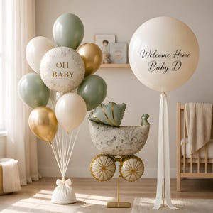 May include: A balloon arrangement featuring sage green, cream, and gold balloons, including a round balloon with the text OH BABY, a pram-shaped balloon, and a large cream balloon with the text Welcome Home Baby. D, all tied with ribbons.