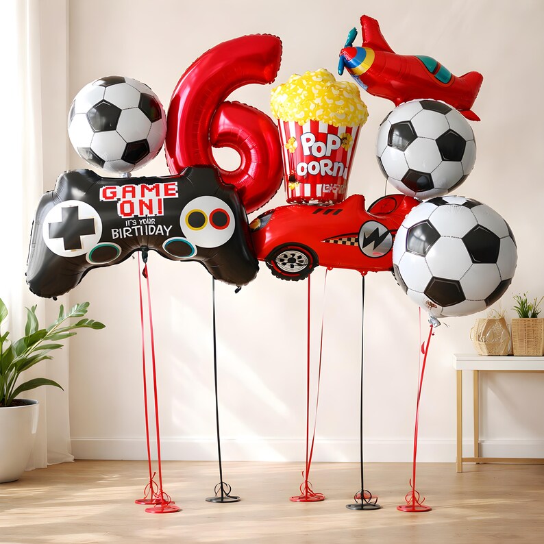 May include: A selection of birthday balloons, featuring a large red number 6, footballs, a video game controller, a race car, a popcorn container, and a red aeroplane. The controller reads "Game On! It's Your Birthday."
