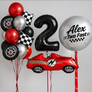 May include: A balloon arrangement featuring a large black number two, a silver balloon with the text Alex Two Fast, a red race car balloon, and several round balloons in red, silver, and black, including two balloons printed with tire designs.