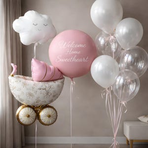 Puede incluir: Una colección de globos para baby shower. Un gran globo rosa con el texto "Welcome Home Sweetheart" está rodeado de globos blancos y transparentes. Un globo en forma de nube y un globo de cochecito completan el arreglo.