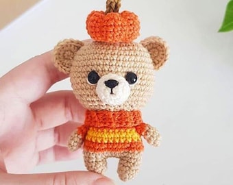 May include: A small crocheted teddy bear wearing an orange and yellow striped sweater and a crocheted orange pumpkin hat.