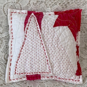 May include: A square, handmade pillow with a patchwork design. The pillow features a white background with a red tree-shaped design in the center, dotted with small red circles. The edges are outlined with red stitching.