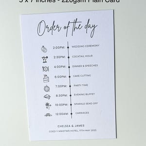 May include: A white card with a black and white order of the day schedule for a wedding. The schedule includes the wedding ceremony, cocktail hour, dinner and speeches, cake cutting, party time, evening buffet, sparkle send off, and carriages. The card also includes the names Chelsea & James and the date 17th May 2025.