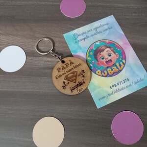Könnte beinhalten: Holzschlüsselanhänger mit einem Superman-Logo und dem Text "PAPA Eres mi super hero favorito leo" auf Spanisch. Der Schlüsselanhänger ist an einem silbernen Schlüsselring befestigt.