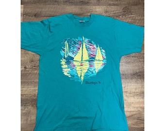 May include: Teal blue t-shirt with a graphic print of three sailboats on a body of water with a reflection. The text "Chincoteague Va." is printed below the graphic.