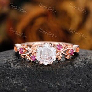 May include: Rose gold engagement ring featuring a hexagonal diamond and pink gemstones set in a delicate floral design.
