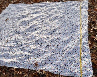 Può includere: Una coperta in tessuto bianco con un motivo ripetuto di lampadine natalizie colorate in rosso, blu, verde e giallo. Un metro a nastro giallo è posizionato lungo il bordo destro, mostrando una lunghezza di circa 152 cm.