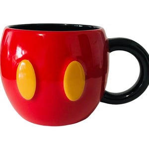 Pu&ograve; includere: Una tazza in ceramica rossa con manico e interno neri. La tazza presenta due forme ovali gialle sul davanti, che ricordano un personaggio dei cartoni animati. La tazza &egrave; lucida e sembra nuova.