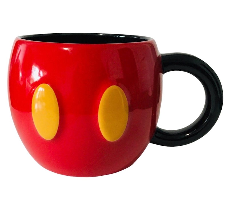 Pu&ograve; includere: Una tazza in ceramica rossa con manico e interno neri. La tazza presenta due forme ovali gialle sul davanti, che ricordano un personaggio dei cartoni animati. La tazza &egrave; lucida e sembra nuova.